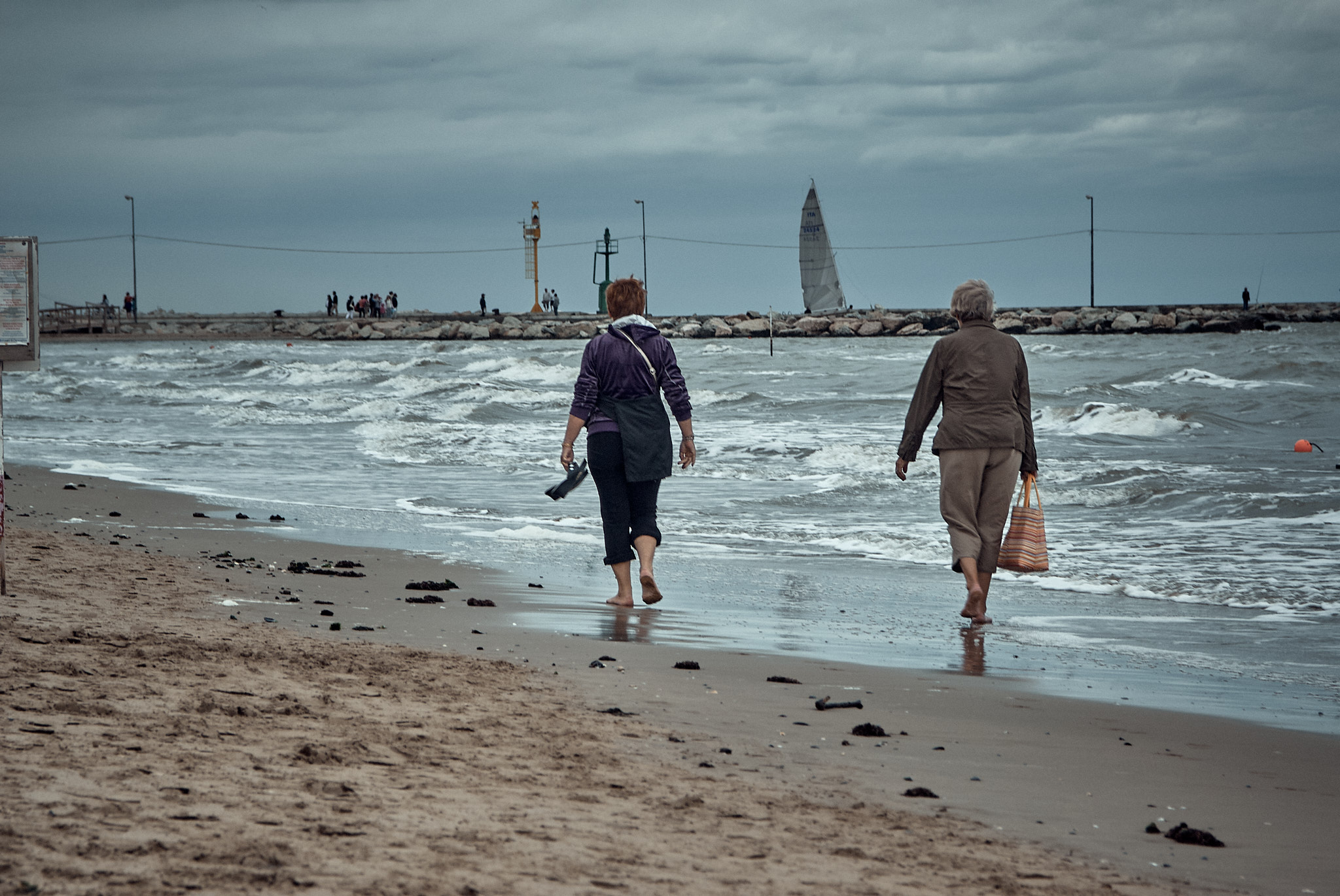 Rimini, barefoot women walking along the shoreline, pier in the background